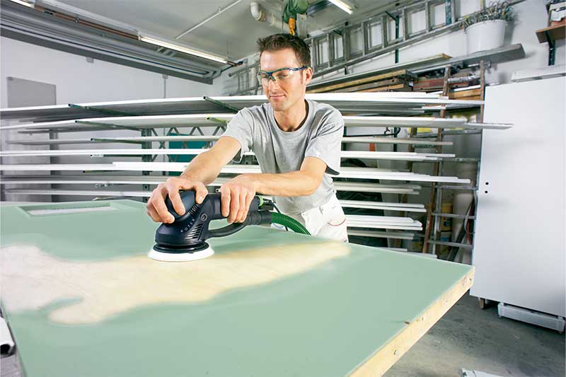 En man slipar en grönlackerad yta