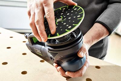 En hantverkare sätter fast slipplattan på en Festool-slipmaskin
