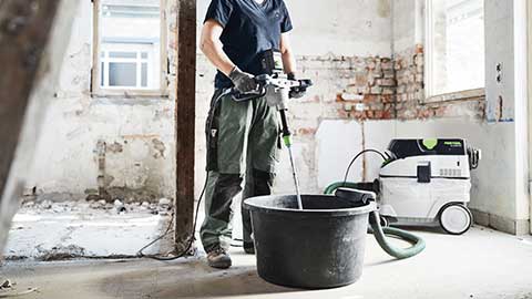 En hantverkare står på en byggarbetsplats och använder en Festool blandare i kombination med en dammsugare.