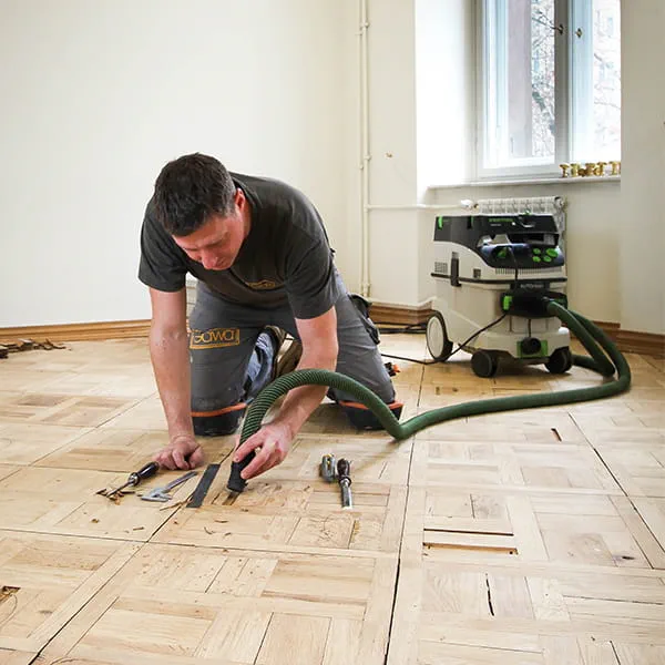 Parkettmästaren Jarek Gawina lossar trasiga bitar från parkettgolvet och tar bort dem med Festool-dammsugaren